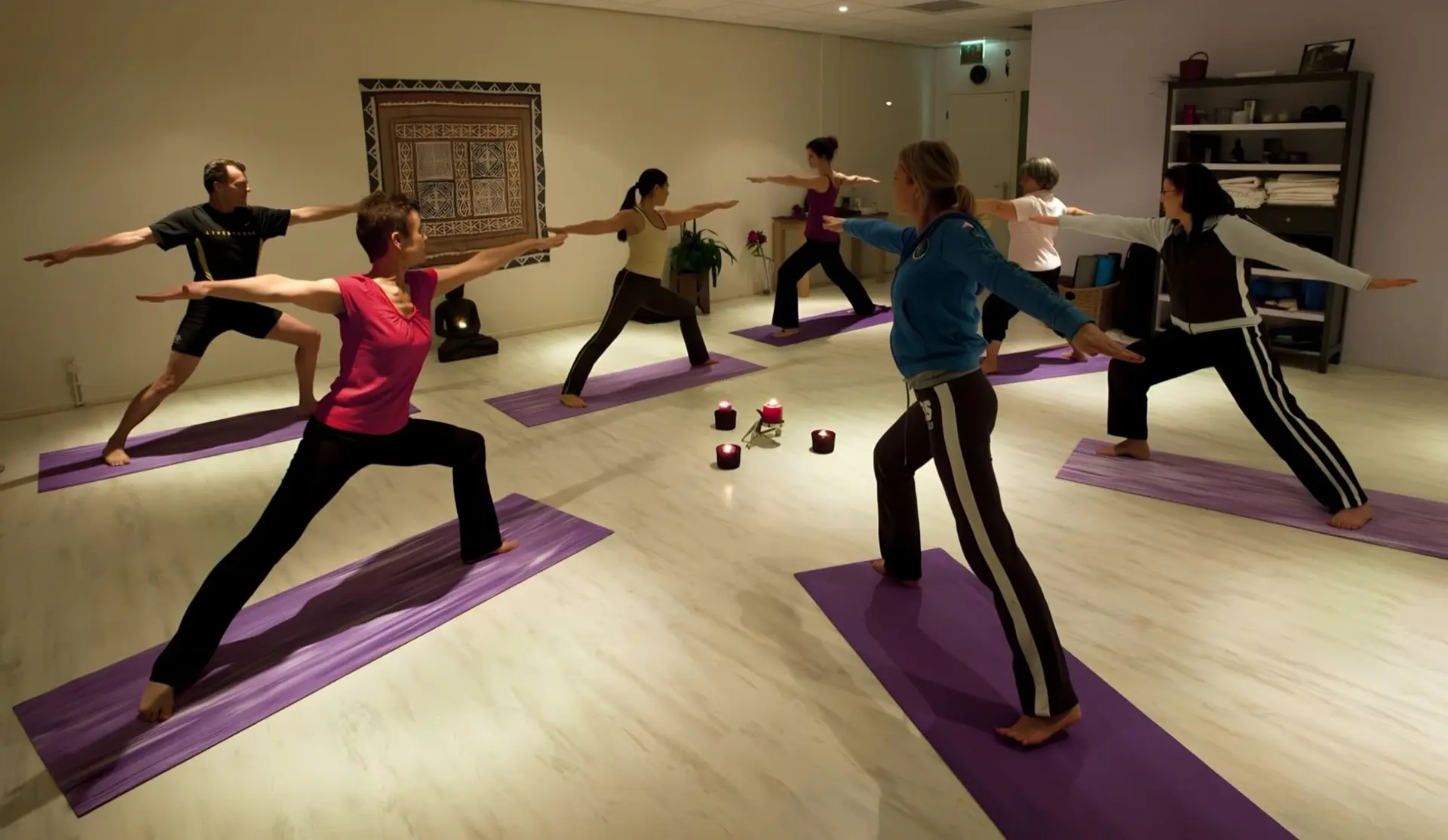 Een les Hatha Yoga bij YogaDebra: de groep in de krijgerhouding rond vier kaarsjes